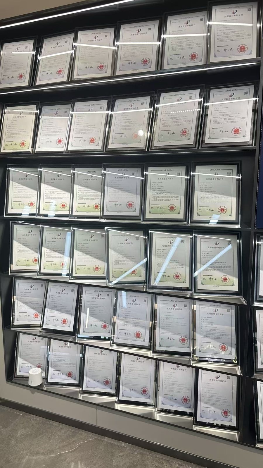 A full wall of framed patent certificates photographed in the showroom